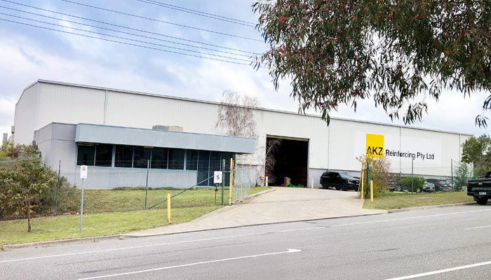 Photo of the AKZ workshop in Hallam. View from the street looking down their driveway at the grey office block on the left and then the large steel shed with their logo on it.
