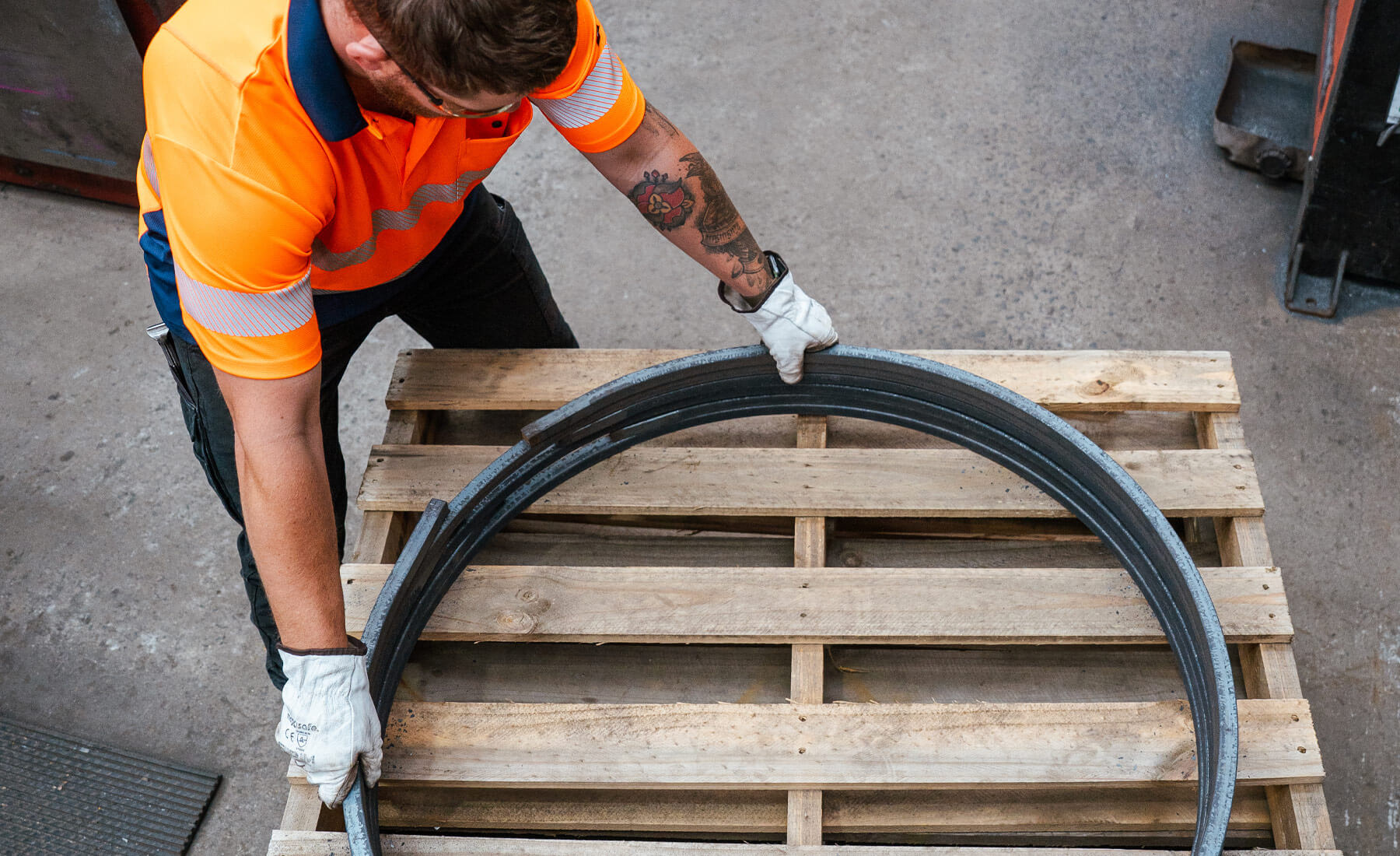 From overhead looking down at a man wearing a high-vis shirt and gloves, aligning a stack of circular steel reinforcing. They are stacked on top of timber pallets.