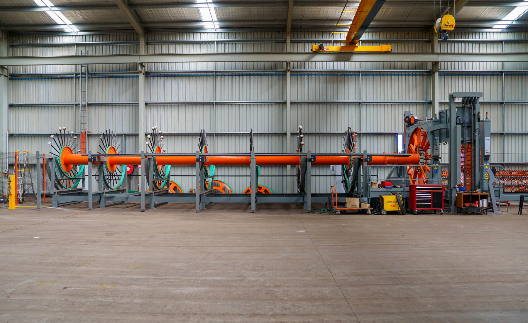 A very complex machine that bends steel reinforcing rods into a column shape. The machine is orange and great and in a clean, new shed.